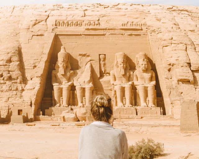 man in gray hoodie standing in front of brown rock formation during daytime